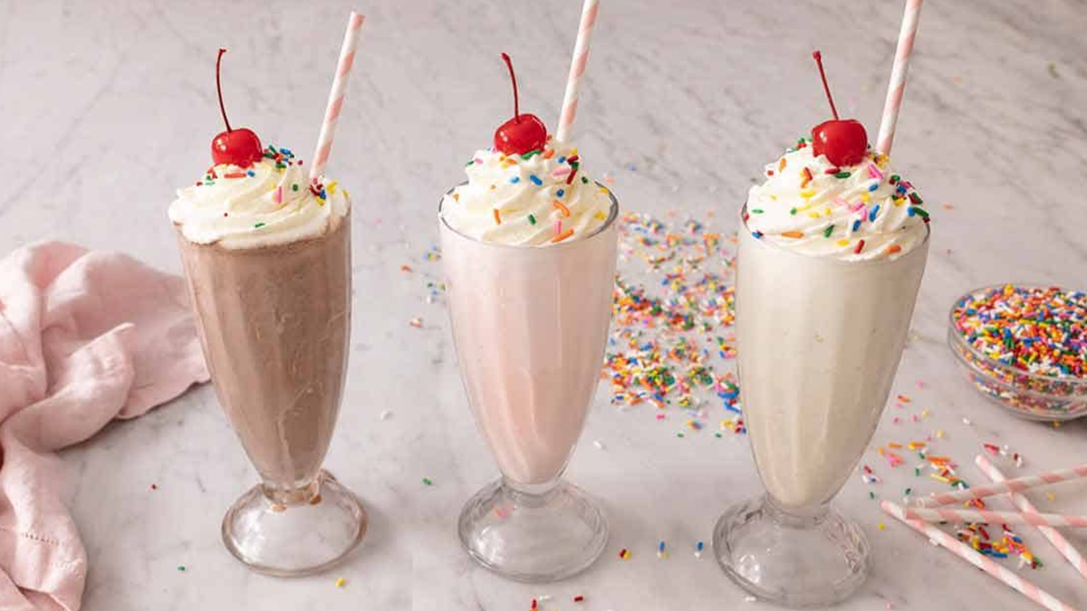 Three colorful milkshakes topped with whipped cream, sprinkles, cherries, and straws.
